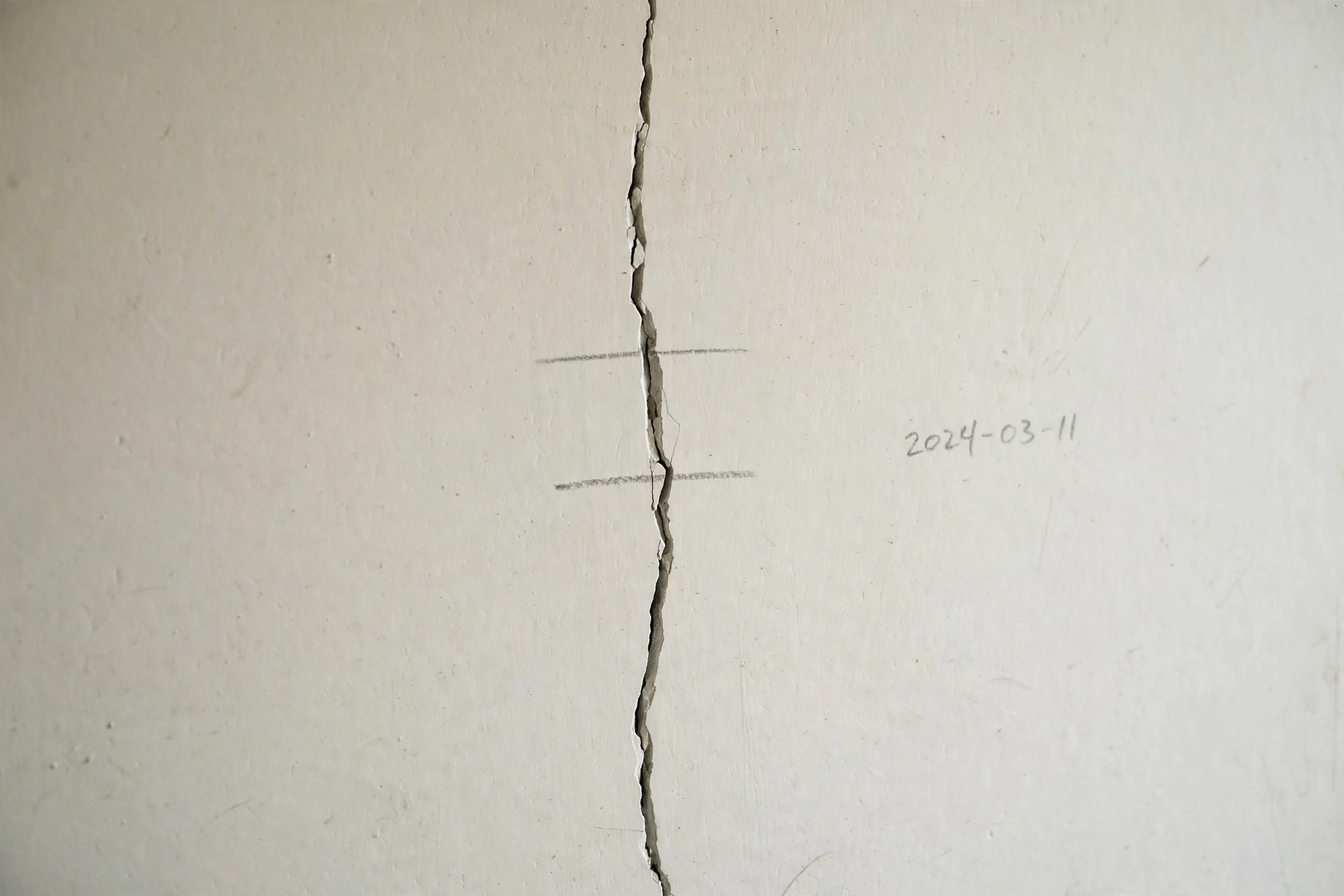 Pencil monitor marks drawn across a crack in a wall